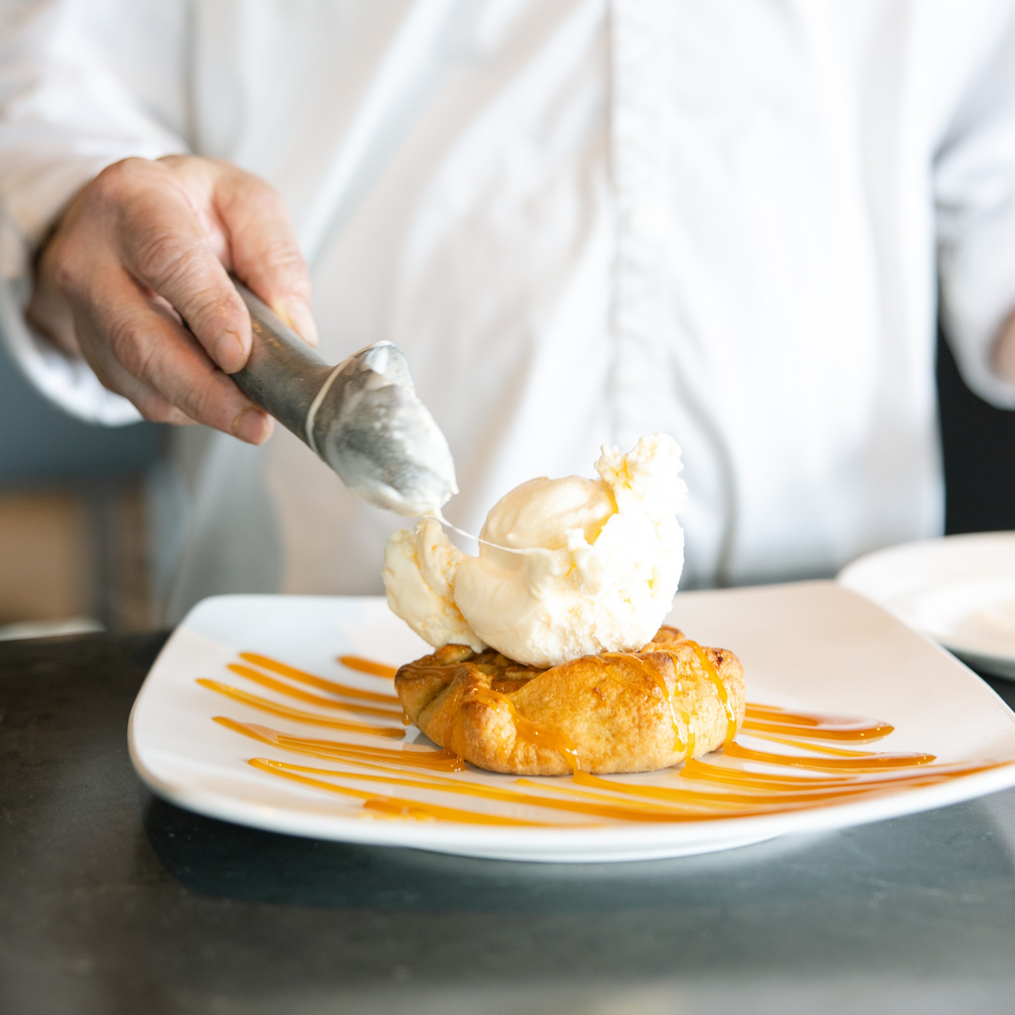 A scoop of vanilla ice cream being served on top of an apple tart over caramel sauce at The Hill Tavern Bar & Grill at Galloping Hill Golf Course in Kenilworth, NJ.